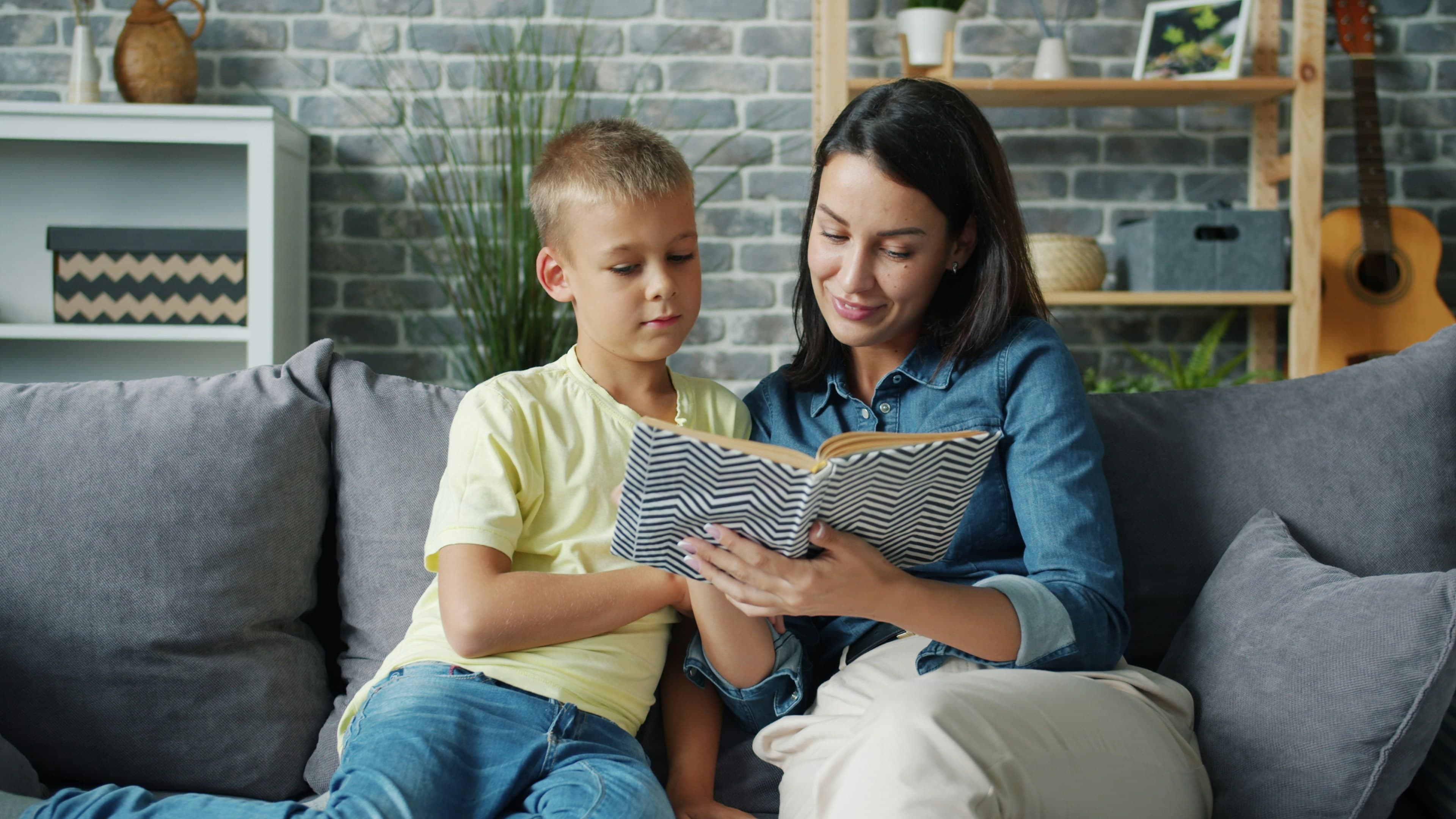 Mother and son reading a book together on sofa.